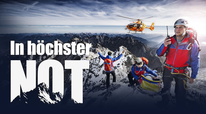 In höchster Not: Drei Angehörige der Bergwacht, die sich mit einer geretteten Person auf einem Berggipfel befinden, weisen einen anfliegenden Hubschrauber ein. Bild: Sender / BR / Timeline Production